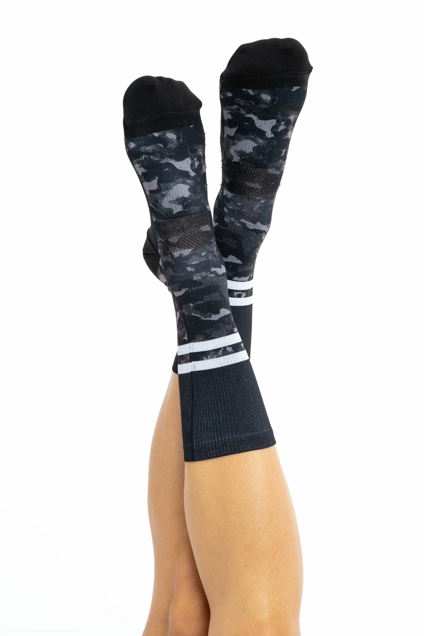 Top view of women’s crew cycling socks with black and grey camo on the bottom and black top with white stripes on a women’s feet.